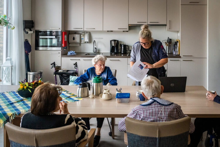 Drie bewoners en een medewerker samen aan tafel in de ontmoetingsruimte.